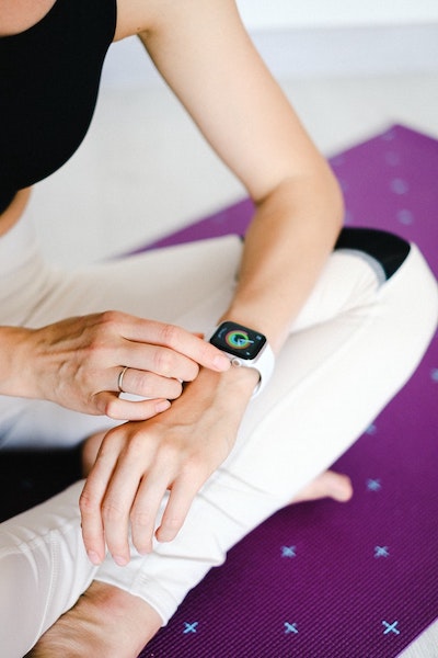 Woman sits on yoga mat and checks her fitness stats on her watch