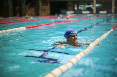 A woman smiles from the middle of a swimming pool while working out doing laps